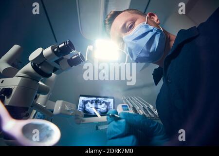 Dentist examining patient with dental equipments against modern dental surgery with x-ray and microscope. Stock Photo