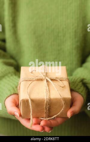 Womans hands holding nice present wrapped in black paper and decorated with green branch, close up Stock Photo