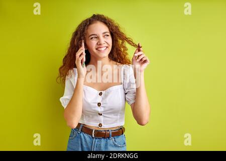 attractive young girl in blouse talk on phone with girlfriend, curly female enjoy sharing news with someone, isolated over green background in studio Stock Photo