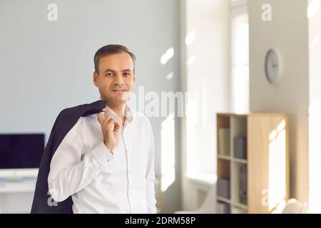 Confident businessman holding jacket over shoulder and looking at camera standing in office Stock Photo