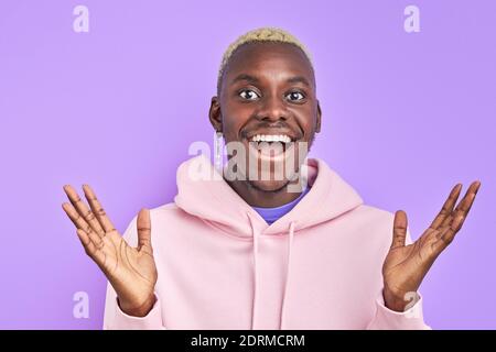 black man is gesturing with hands after getting news, he is surprised, stand with opened mouth. isolated on purple background. portrait in studio Stock Photo