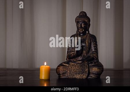 Buddha statue with burning candle on wooden table with soft textured background and dark environment. Spirituality, buddhism and religion concepts Stock Photo