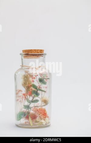 Dried flowers and potpourri in a glass jar with a cork on a white table Stock Photo