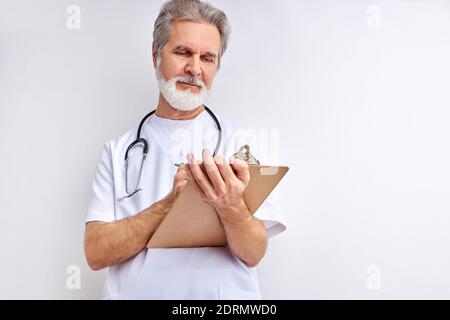 senior doctor taking medical history of patient, make notes, write in tablet, use stethoscope. stand posing isolated over white studio background Stock Photo