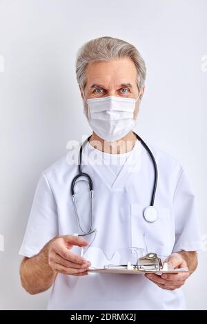 portrait of nice professional bearded man pharmacy expert in mask with stethoscope, isolated on light white color background Stock Photo