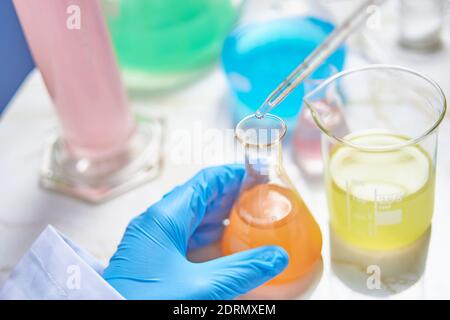 lab technician wearing blue gloves doing experiments and tests in a lab with different colored substances Stock Photo