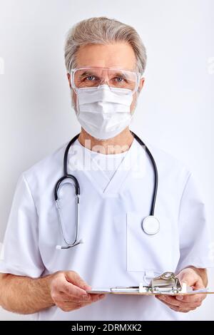 doctor man talks about the diagnosis, holding tablet in hands and wearing protective medical mask, isolated on white background Stock Photo