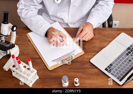 top view on cropped doctor making notes sitting at table, make research with test tubes of coronavirus, using laptop Stock Photo