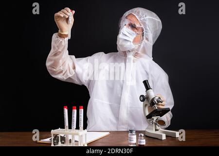 male scientist is testing a sample of biological tubes contaminated by Corona-virus Covid 19, using microscope Stock Photo