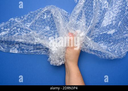 female hand holding crumpled piece of polyethylene with air bubbles on a blue background, packing material Stock Photo