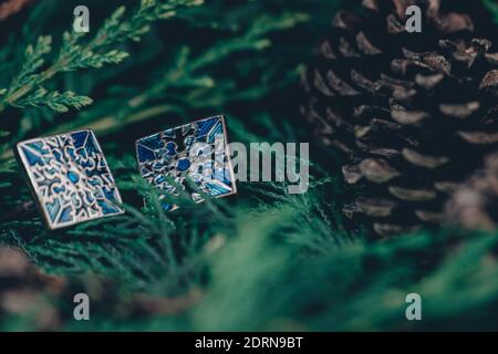 Thame,UK - 25 Nov 2020: Blue cufflinks in silver on evergreen and pinecones background, snowflake pattern on each cufflink, christmas mens jewellery Stock Photo