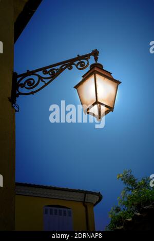 Illuminated old iron lantern on the wall at night. Vintage outdoor lamp. Stock Photo
