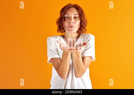 woman blow kiss at camera,redhead lady share love with everyone, isolated over orange background Stock Photo