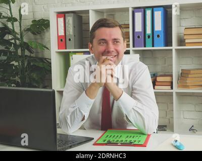 Smiling young employee at table. The man was daydreaming at his workplace. Stock Photo
