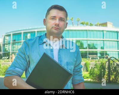 Portrait of young attractive man with a laptop in the summer on the street. Stock Photo