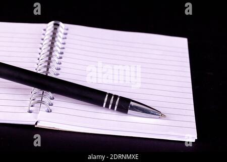 Pen and opened A5 notepad with white lined pages and spiral bound with a black background Stock Photo