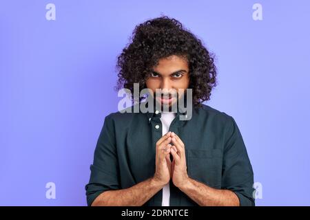 sly curly male conceived something, thinking about idea, look at camera head down, isolated over purple background Stock Photo