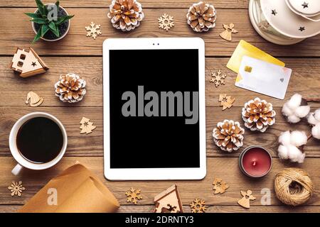 Tablet with black screen, cup of coffee, debit card, Xmas decor, snowflakes on wooden table Top view Flat lay Holiday shopping list, Happy New Year Stock Photo