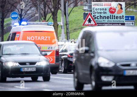 Cologne, Germany. 21st Dec, 2020. Motorists wait outside the Corona quick test drive-in at the Lanxess Arena while an emergency ambulance drives past. Motorists can be tested directly in their cars in a parking garage at the arena. Credit: Marius Becker/dpa/Alamy Live News Stock Photo