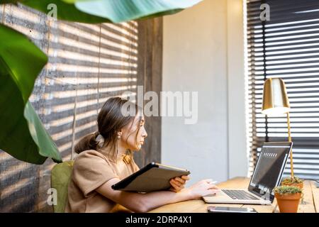 Creative woman in comfortable domestic suit working on digital tablet at the cozy and style home office Stock Photo