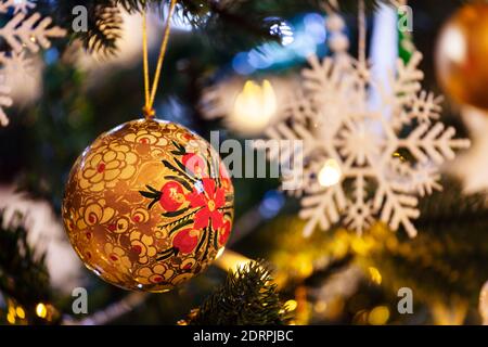 Golden christmas bauble hanging on a Christmas tree, with lights and decorations in the background. Stock Photo