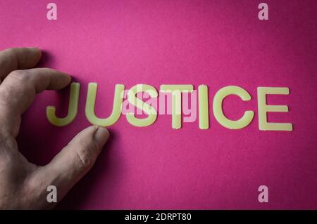 Human fingers holding the word Justice written with plastic letters on bright pink paper background, concept Stock Photo