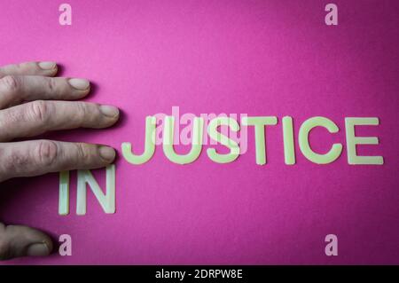 Human fingers sliding two letters to the word Injustice to make it Justice, written with plastic letters on a bright pink paper background, concept Stock Photo