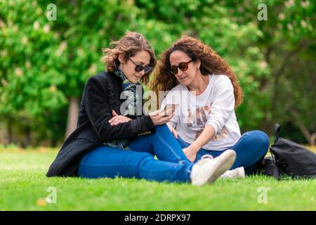 Talking and studying, with phone, relaxed in the park, sitting on the grass. Stock Photo