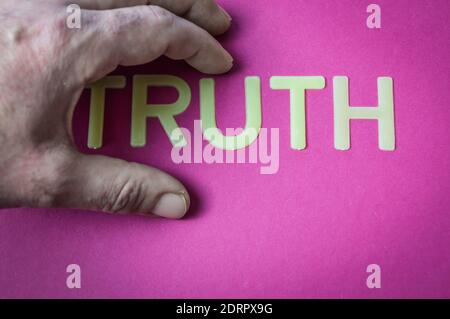 Human hand hiding the word Truth written with plastic letters on a bright pink paper background, concept Stock Photo