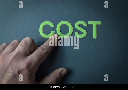 Human finger pointing the word Cost written with plastic letters on dark gray paper background, concept Stock Photo
