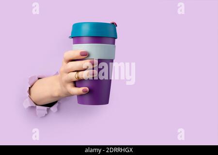 Woman's hand through a hole in the paper holds a reusable cup. Eco friendly living. Zero waste concept. Take away drink coffee tea to-go Stock Photo