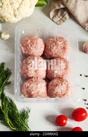 Raw meatballs and meatballs on a plastic substrate surrounded by fresh vegetables, herbs and spices.  Stock Photo
