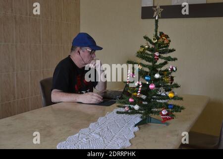Elderly man, at Christmas time, working on notebook in home office on marble table, with Christmas tree, Brazil, South America Stock Photo