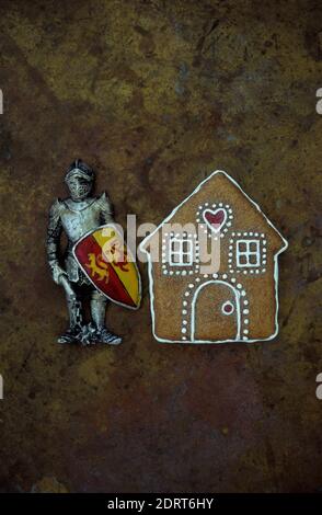 Model of gingerbread house with model of medieval knight in armour standing beside it