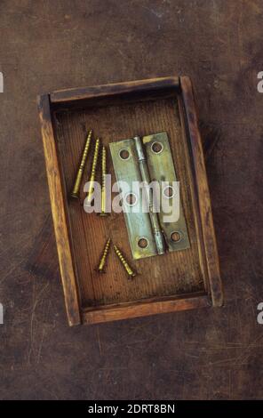 Small old wooden box containing tarnished brass door hinge and used brass screws Stock Photo