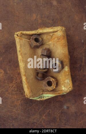 Old crumpled rust-stained cardboard box with three rusty metal nuts and used screw lying on top Stock Photo