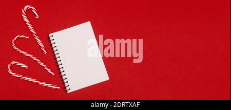 Flatlay at white sheets of notebook and Christmas candies at red background Stock Photo