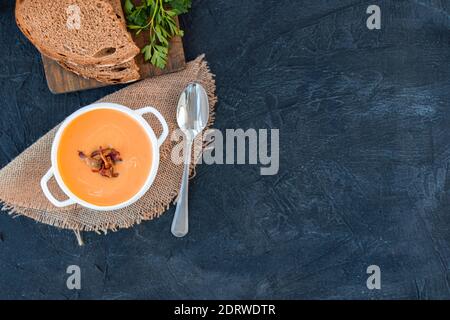 Pumpkin soup with fried bacon in white plate on a black background with bread and parsley. Top view. Copy cpase Stock Photo