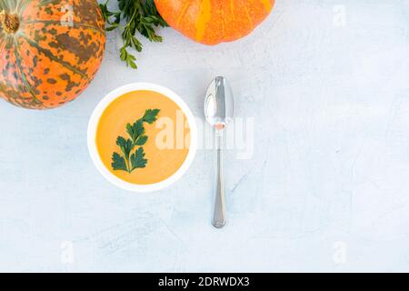Pumpkin and carrot soup with cream and parsley in a white plate on white background with pumpkins. Top view. Copy space Stock Photo
