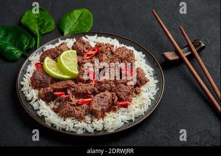 Beef Rendang on black plate at black slate table top. Indonesian padang cuisine meat dish. Asian food. Stock Photo