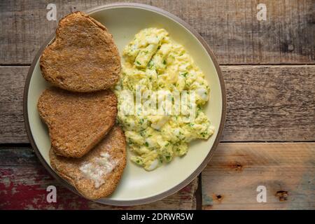 A portion of scrambled eggs with parsley served with heart shaped toasted brown bread. England UK GB Stock Photo