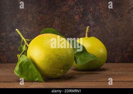 horizontal view in foreground of two grapefruits with leaves on a wooden table Stock Photo