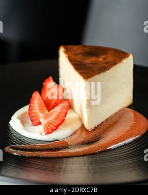 Cheese cake decorated with fresh strawberries and jam on black plate. Selective focus, close up Stock Photo