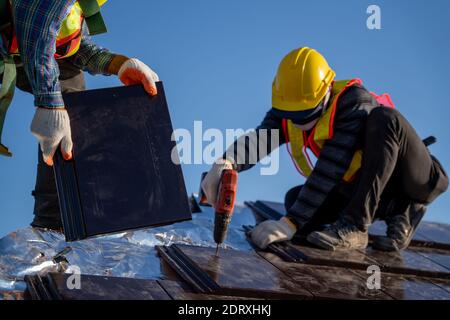 Close up worker install new ceramic tile roof with Roofing tools Electric drill used in the construction site. Stock Photo