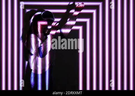 Woman using virtual reality headset, moving hand at interactive technology exhibition with multicolor projector light illumination, immersive concept Stock Photo