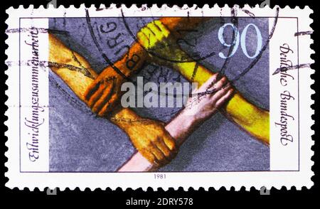 MOSCOW, RUSSIA - FEBRUARY 20, 2019: A stamp printed in Germany, Federal Republic, shows Arms of different Races forming Square, Co-operation with Deve Stock Photo