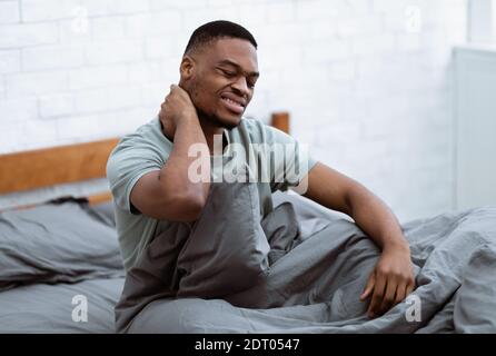 African Guy Suffering From Neck Pain Waking Up In Bedroom Stock Photo