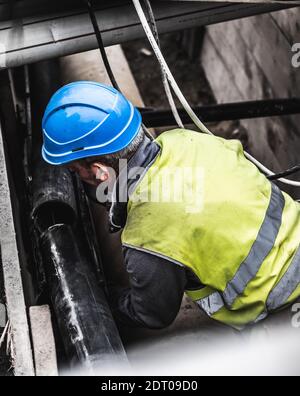 Pipe fitter in yellow uniform working on a construction site. Worker fitting pipes underground, Geneva, Switzerland. Stock Photo