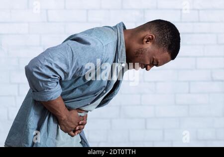 Black Man Suffering From Stomachache Standing Over White Wall, Side-View Stock Photo