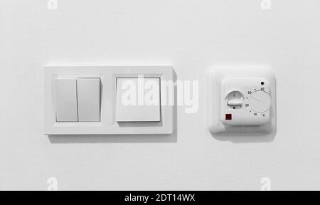 Pair of simple light switches with dimmer. Inexpensive plastic mechanical double switch with thermostat against white wall. Old air conditioner Stock Photo
